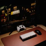 Close-up of a gaming desk setup featuring a keyboard, controller, and monitor at night.