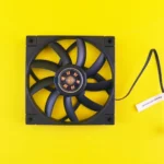 A black computer fan with a cable against a vibrant yellow backdrop, ideal for tech themes.