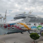 Vibrant Norwegian Pearl cruise ship docked at an industrial port under a cloudy sky.